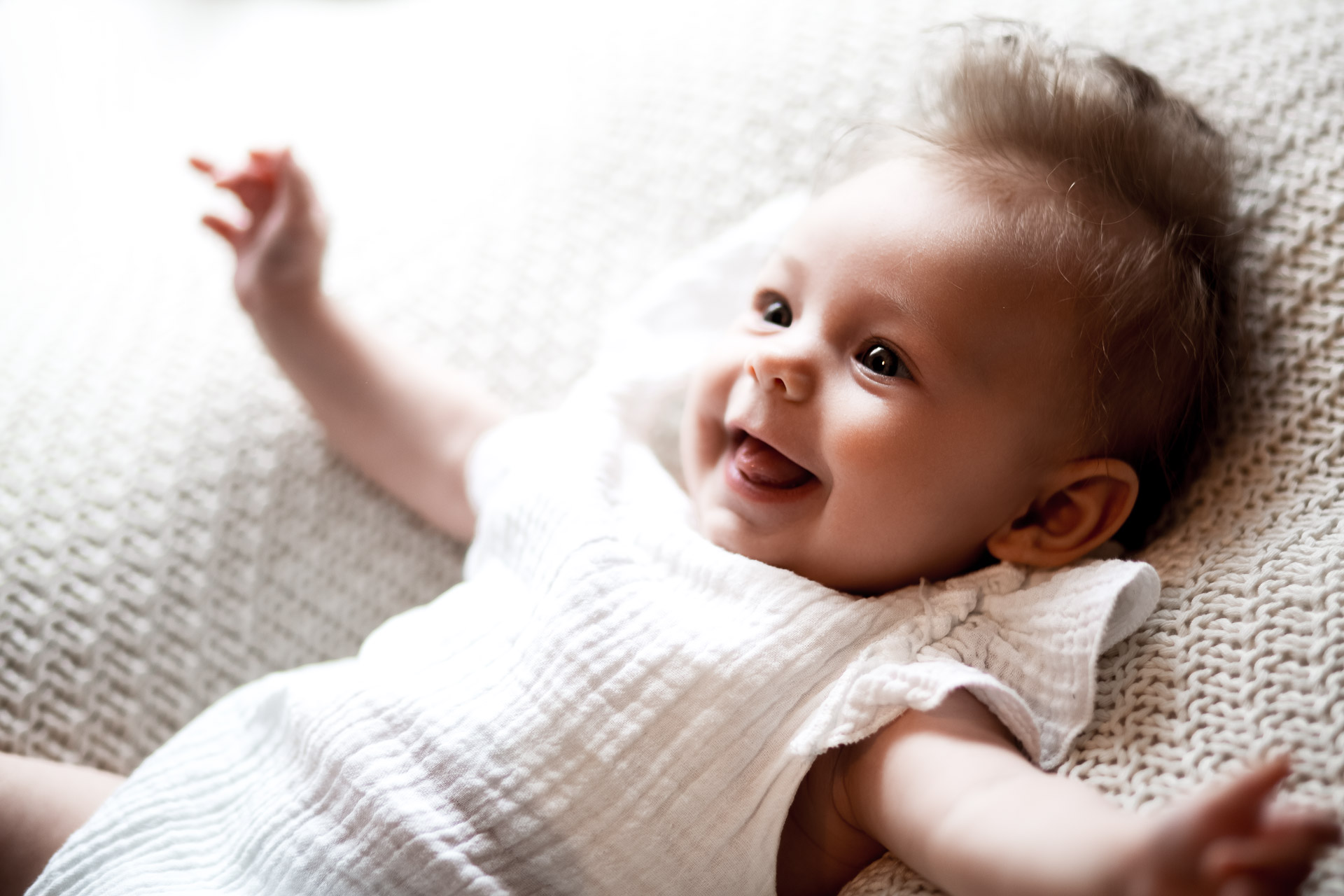 Babyshooting in weiß Baby in weißem Body lacht und strahlt und breitet die Arme aus