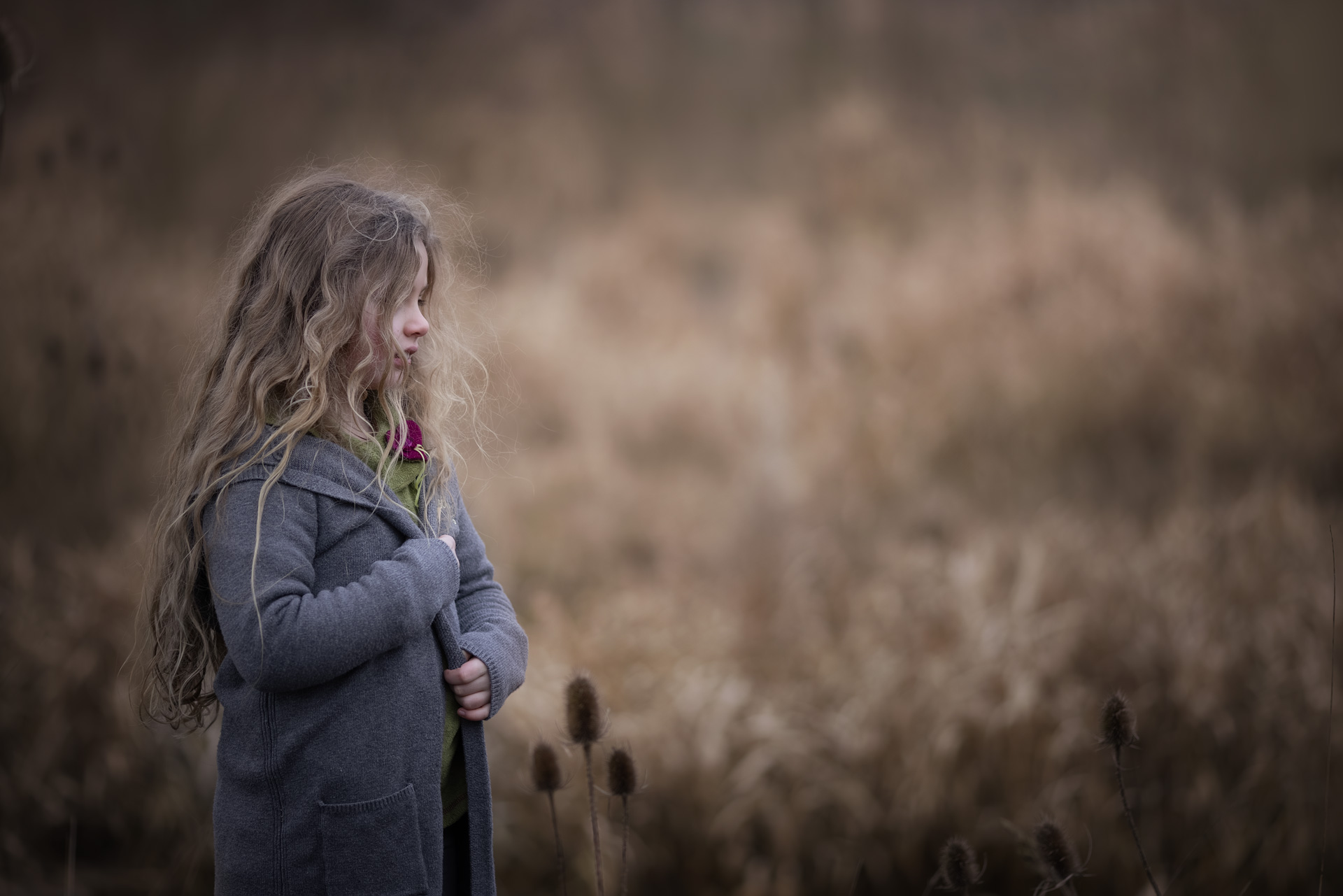 Kindershooting in der Natur-Yvonne Pesch Fotografie Mädchen in grauem Strickmantel mit langen offenen blonden Haaren steht in der Natur